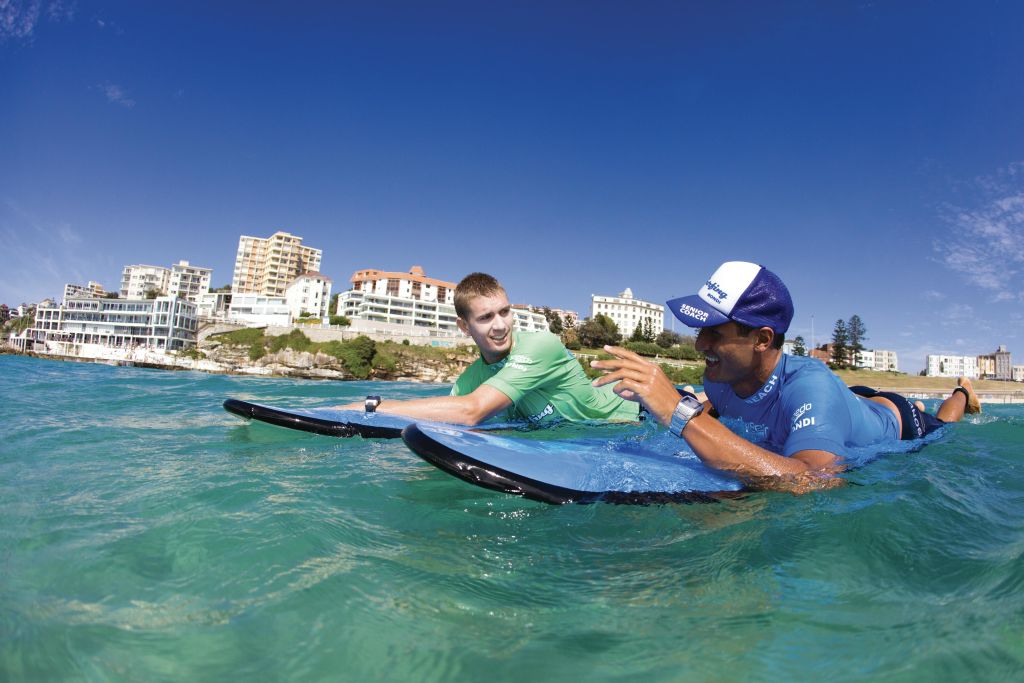 해안 도시 근처 바다에서 두 사람이 서핑보드를 타고 맑고 푸른 하늘 아래 대화를 나누고 있습니다.