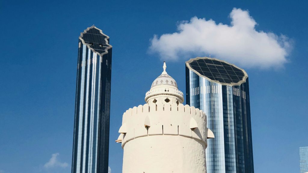 전면에 돔형 탑이 있고, 뒤에는 현대적인 유리 고층 건물이 있으며, 위에는 구름이 있는 푸른 하늘이 있습니다.