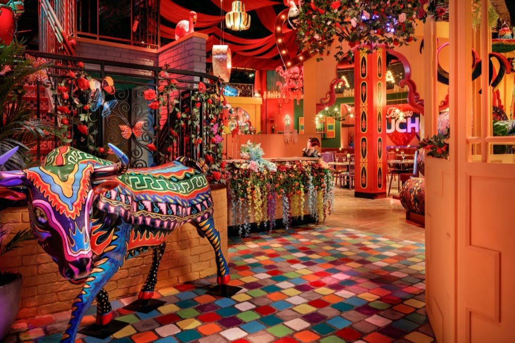 모자이크 바닥, 장식된 소 동상, 등불, 식물, 식탁을 배경으로 활기차고 다채로운 인테리어가 돋보입니다.