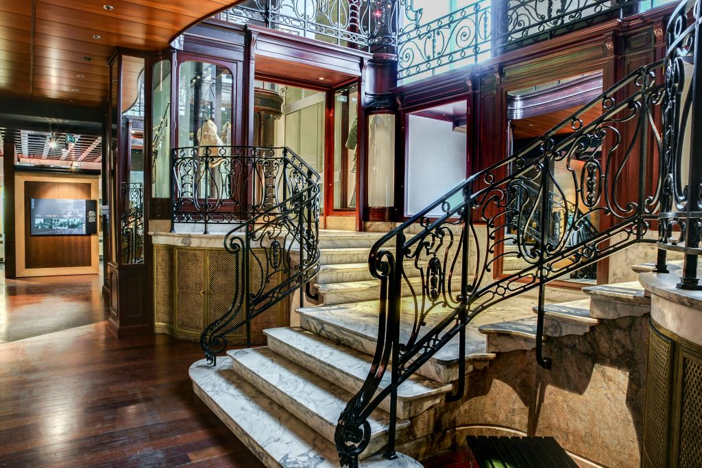 대형 거울이 있는 고급스러운 목재 패널 내부에 정교한 연철 난간이 있는 우아한 대리석 계단.