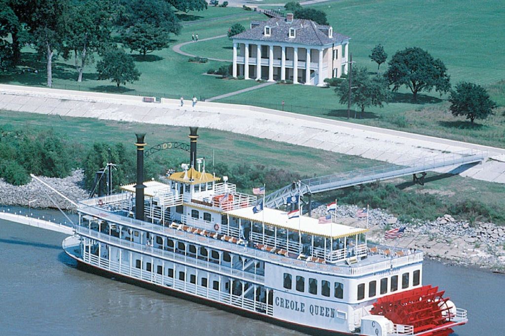 '크리올 퀸' 이라는 이름의 강물이 커다랗고 하얀 대농장 주택과 푸른 잔디밭을 배경으로 강 위에 떠 있습니다.