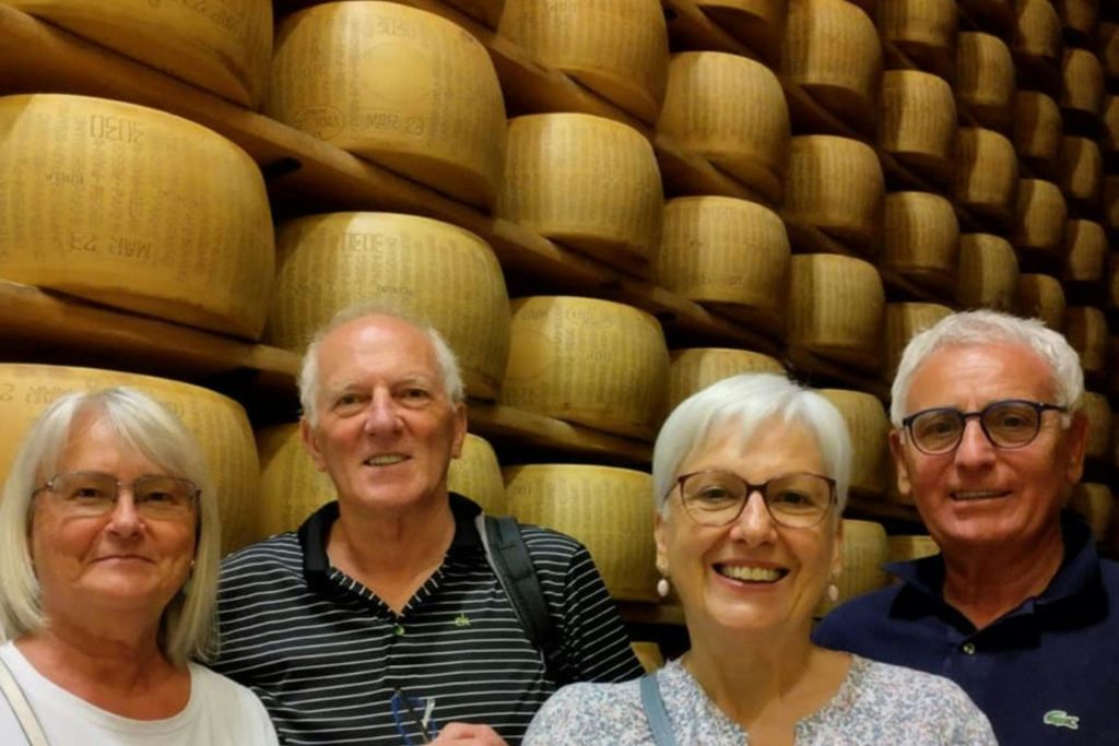 치즈 바퀴 더미 앞에서 세 명의 노인이 미소를 짓고 있습니다.