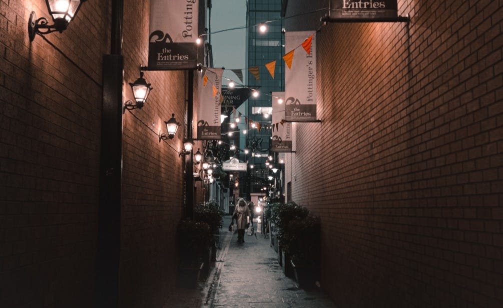 현악기, 현수막, 벽등, 카메라를 향해 걸어가는 사람이 있는 좁은 골목길. 황혼이 질 무렵의 도시 환경.