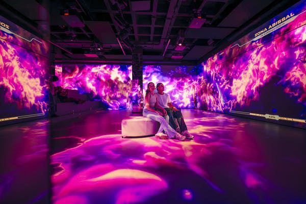 벽과 바닥에 선명하고 화려하며 추상적인 디지털 투영이 있는 방의 벤치에 앉아 있는 두 사람.