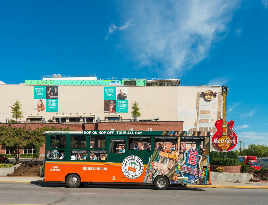 화창한 날 하드록 카페 간판 옆에 포스터가 붙은 건물 앞에 주황색과 녹색 투어 버스가 있습니다.