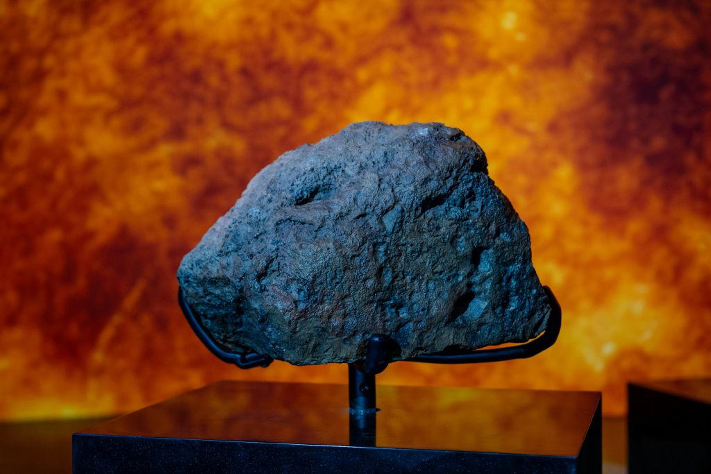 불타는 주황색 배경을 배경으로 스탠드에 어두운 질감의 바위가 전시되어 있습니다.
