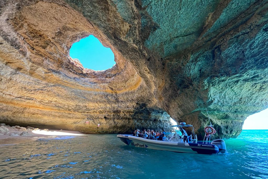 꼭대기에 커다란 원형 개구부가 있고 하늘을 볼 수 있으며 작은 해변이 보이는 동굴 안에 사람들이 있는 보트입니다.