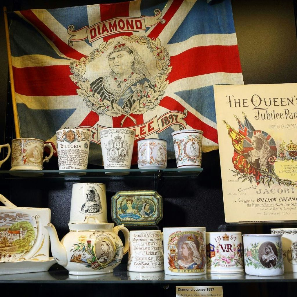 빅토리아 여왕의 다이아몬드 기념일을 기념하는 세라믹 머그잔과 기념품이 Union Jack 깃발과 포스터와 함께 전시되어 있습니다.