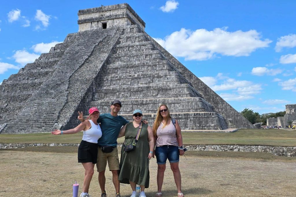 화창한 하늘 아래 커다란 석조 피라미드 앞에서 포즈를 취하는 네 사람.
