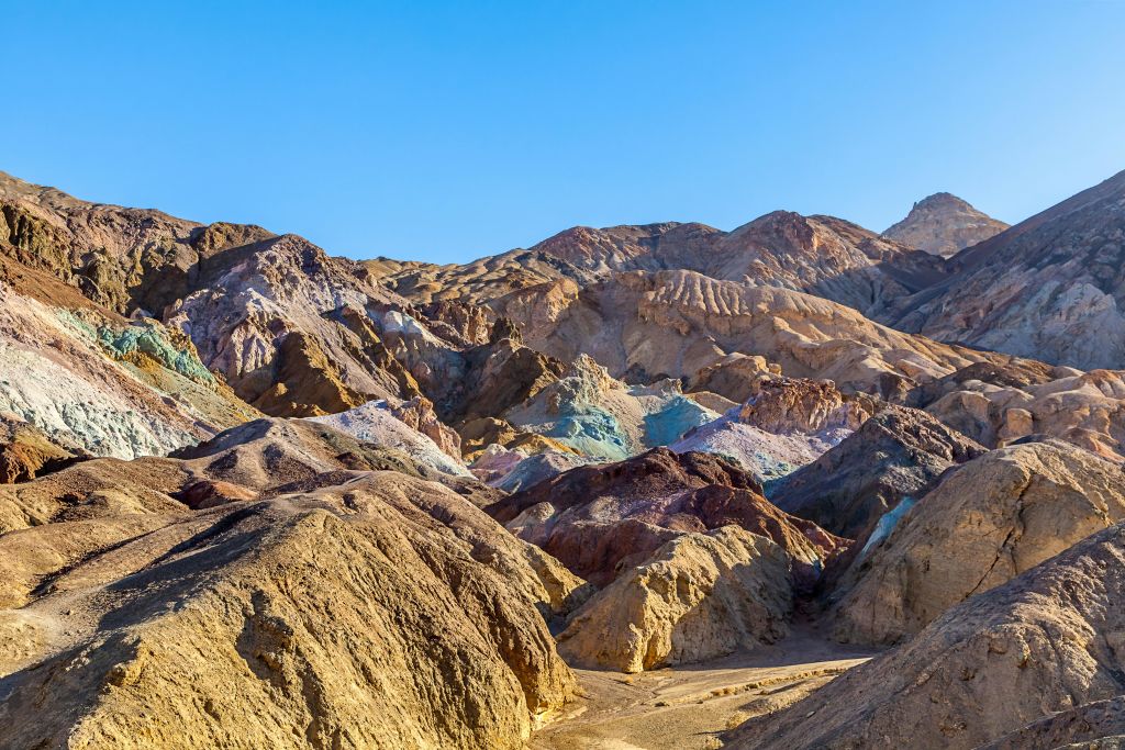 갈색, 분홍색, 보라색, 녹색의 음영을 보여주는 맑고 푸른 하늘 아래 다채롭고 층층이 쌓인 바위 지층.