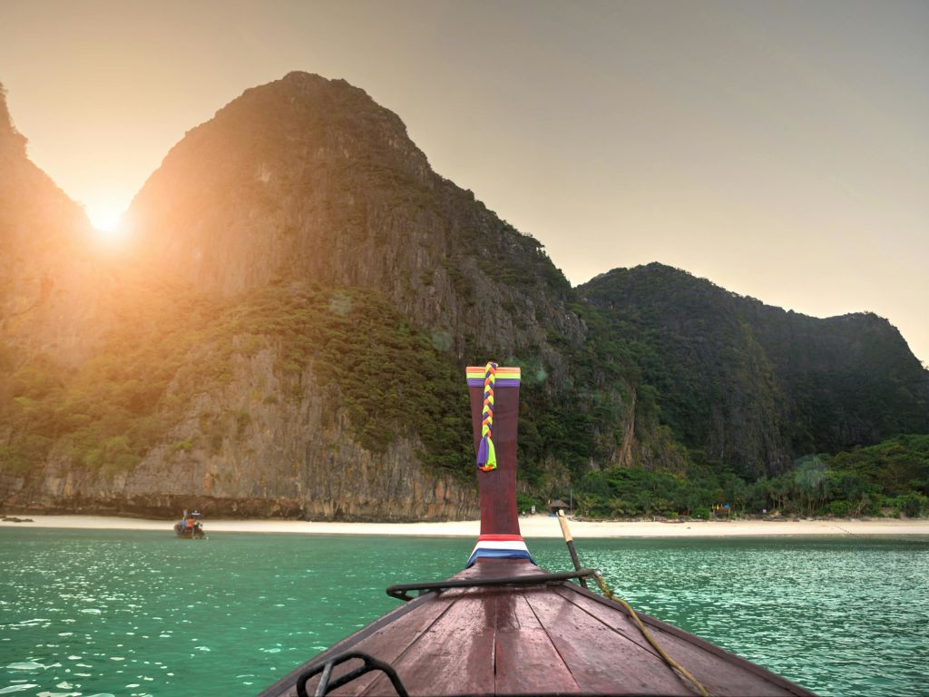 울창한 푸른 언덕과 햇살이 내리쬐는 모래사장에 롱테일 보트가 다가옵니다.