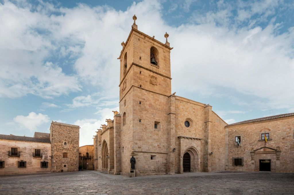 부분적으로 흐린 하늘 아래 자갈과 인근 건물로 둘러싸인 종탑이 있는 유서 깊은 석조 교회.