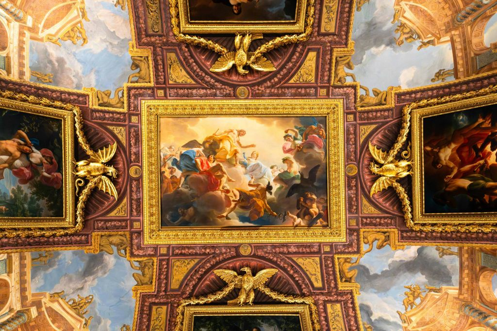 화려한 골드 액센트로 둘러싸인 신화적 장면을 묘사한 중앙 액자 그림이 있는 풍부하게 장식된 천장.
