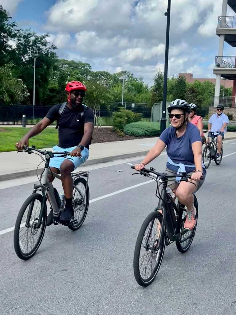 도시 거리에서 자전거를 타고 헬멧을 쓰고 녹지와 건물을 배경으로 한 무리의 사람들.