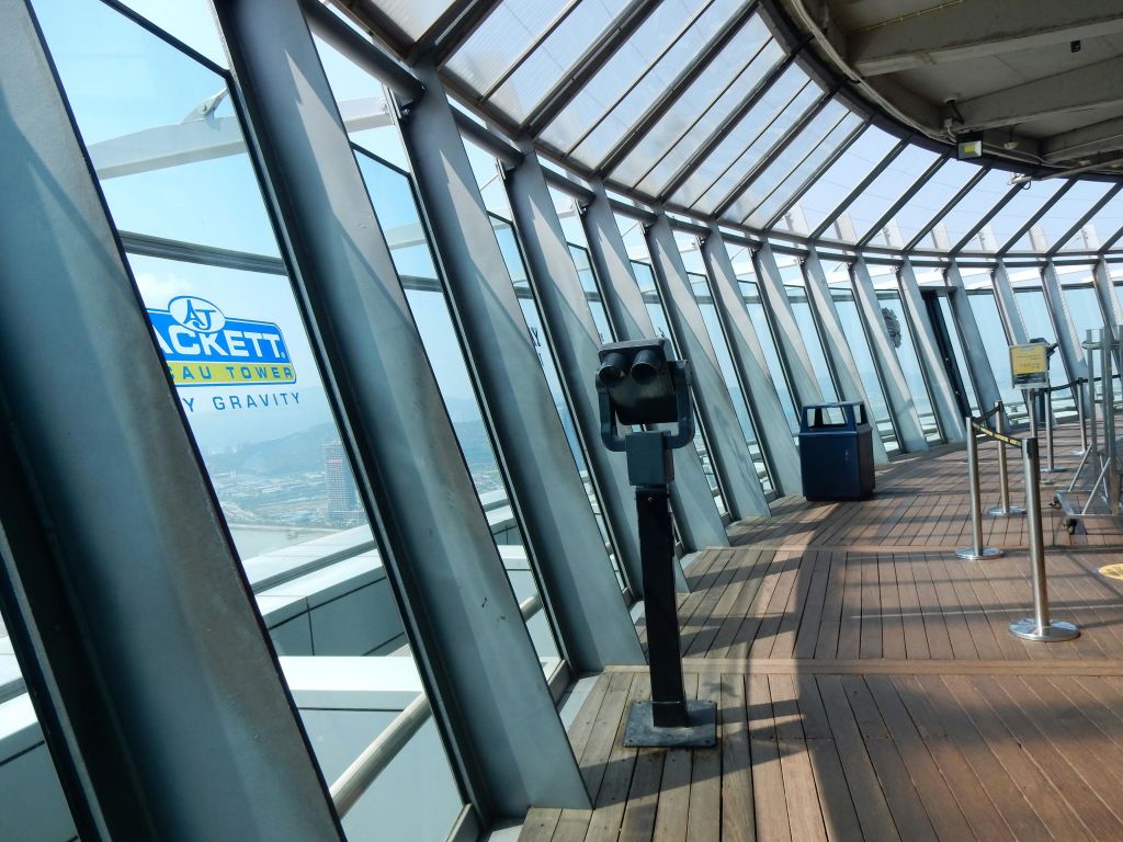 망원경, 커다란 유리창, 나무 바닥이 있는 전망대. "AJ Hackett Macau Tower Skywalk X" 라는 표지판이 있습니다.