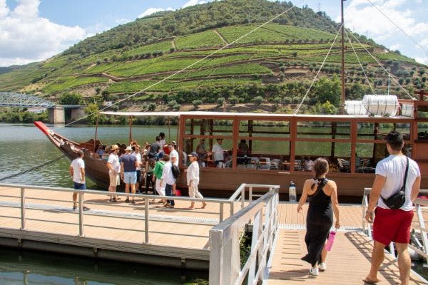 맑고 푸른 하늘 아래 포도밭으로 덮인 언덕을 배경으로 선착장에서 나무 보트를 타는 사람들.