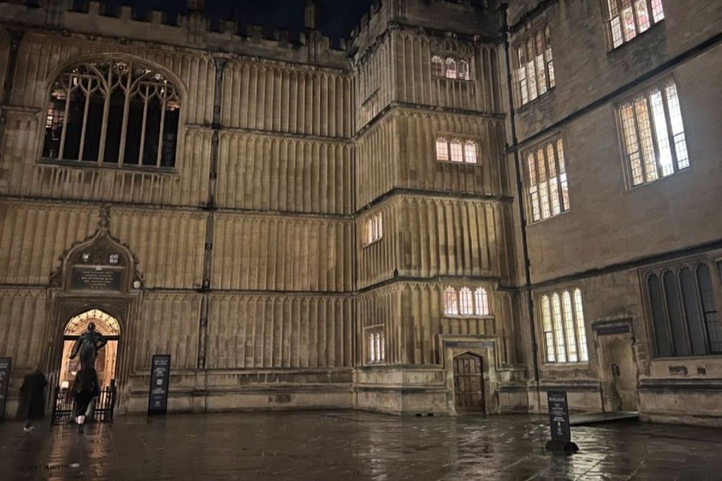 정교한 건축 디테일과 젖은 마당이 특징인 역사적인 석조 건물로 밤에는 조명이 켜진 창문이 있습니다.