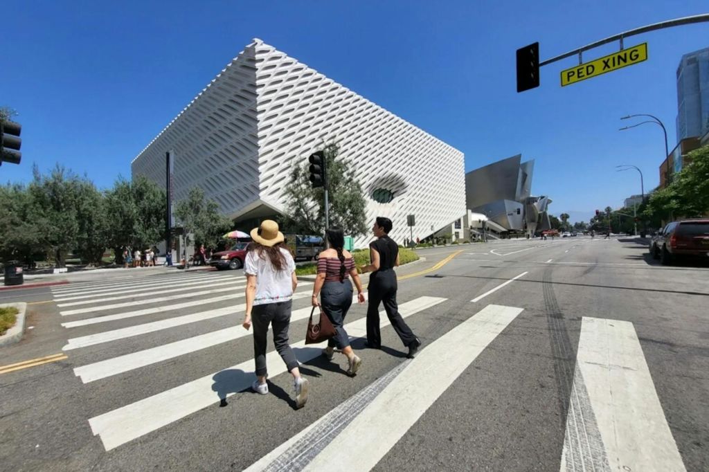 현대적인 흰색 건물과 신호등이 배경으로 보이는 횡단보도에서 거리를 가로지르는 세 사람.