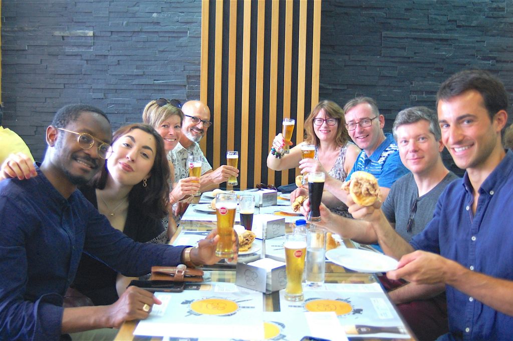 6명의 일행이 미소를 지으며 테이블에서 맥주잔을 들고 현대적인 인테리어가 돋보이는 레스토랑에서 햄버거를 즐깁니다.