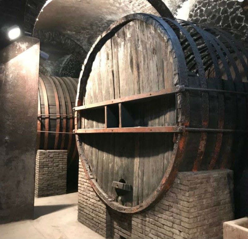 조명이 희미한 지하실에 금속 밴드와 석재 지지대가 있는 대형 나무 통.