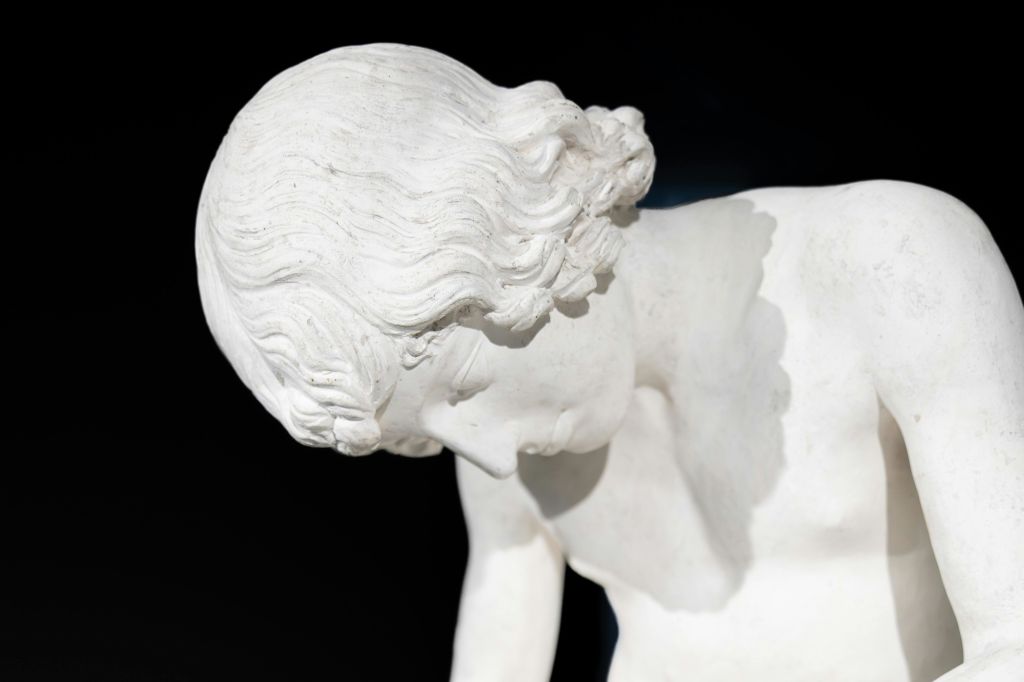 곱슬머리를 하고 어두운 배경을 바라보는 하얀 대리석 조각상의 클로즈업.