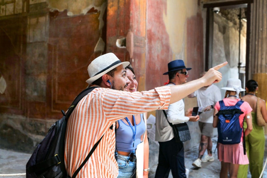 한 무리의 관광객과 함께 유적지를 탐험하면서 웃으며 가리키고 있는 남성과 여성.