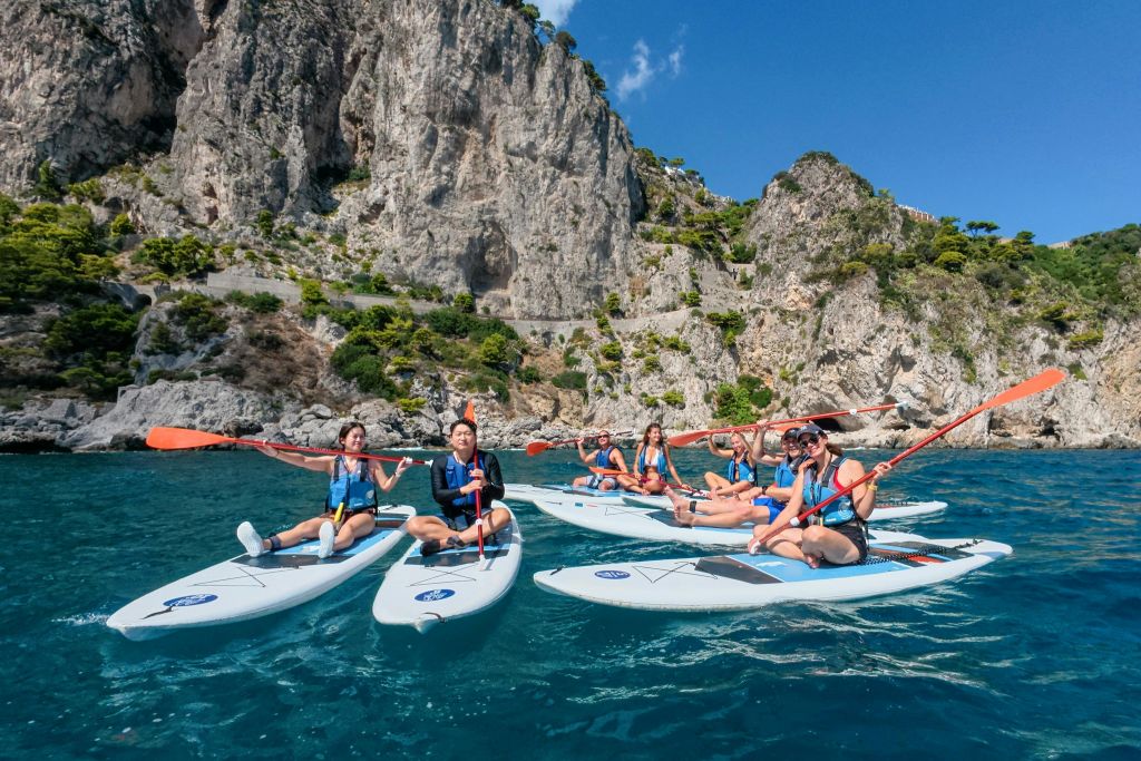 맑고 푸른 하늘 아래 바위 해안선 근처의 청록색 바다에서 카약을 타는 한 무리의 사람들.
