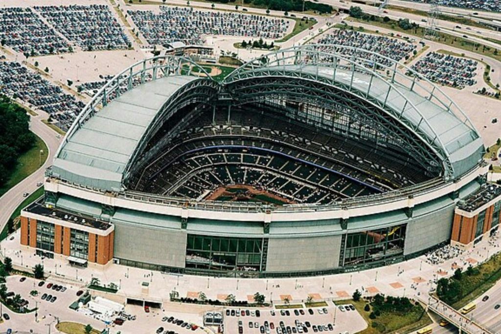 주차장 및 녹지로 둘러싸인 부분적으로 개방된 접이식 지붕이 있는 경기장의 공중 전망.