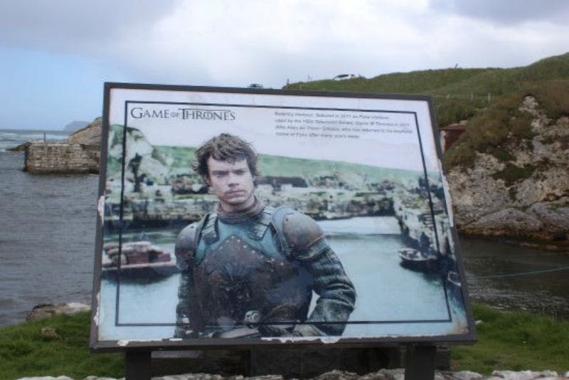 "왕좌의 게임" 표지판에는 아름다운 수변 유적을 배경으로 갑옷을 입은 캐릭터가 표시됩니다.