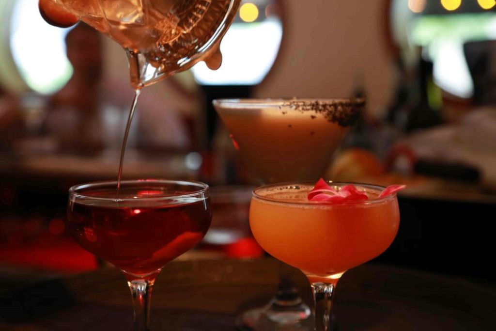 세 가지 칵테일 컬렉션으로, 하나는 셰이커에서 부어지고 다양한 색상의 음료와 장식이 우아한 잔에 담겨 있습니다.