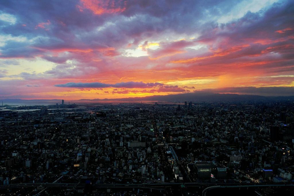 주황색, 분홍색, 보라색 구름으로 가득한 생동감 넘치는 하늘과 함께 석양을 감상하며 도시의 스카이라인을 즐겨보세요. 먼 산이 보입니다.