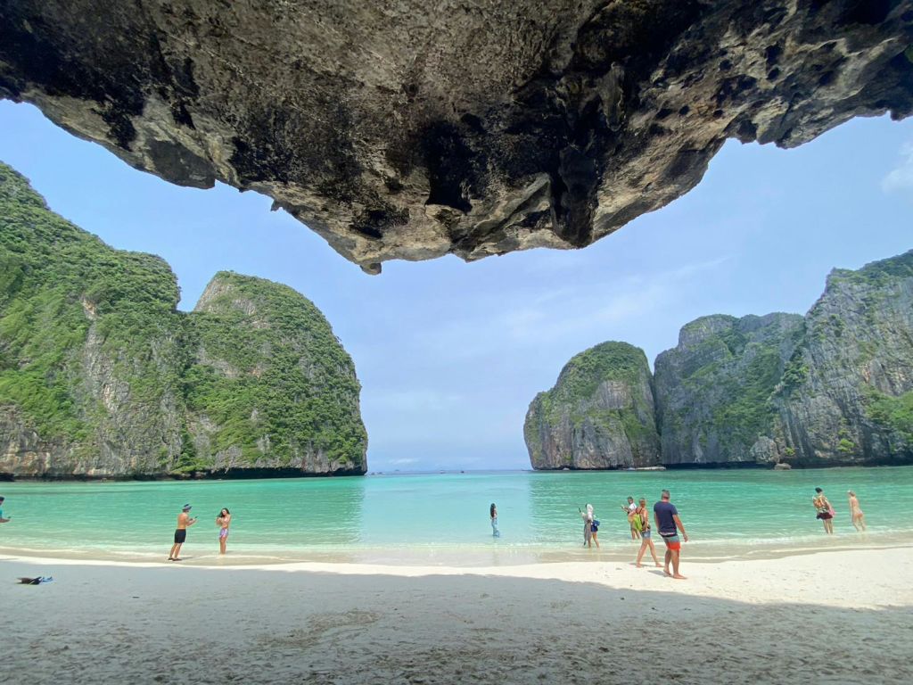 그늘진 동굴 개구부에서 바라본 석회암 절벽을 배경으로 맑고 얕은 석호를 즐기는 관광객들.