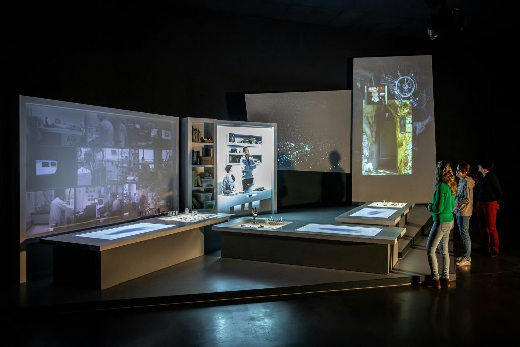 어두운 방에 다양한 비주얼, 물품이 놓인 선반, 조명 테이블을 보여주는 화면이 있는 미래형 디스플레이 설정입니다.