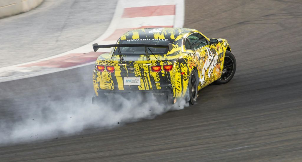 활기가 넘치는 노란색 경주용 자동차가 트랙에서 드리프트를 수행하여 타이어에서 연기 흔적을 만듭니다.