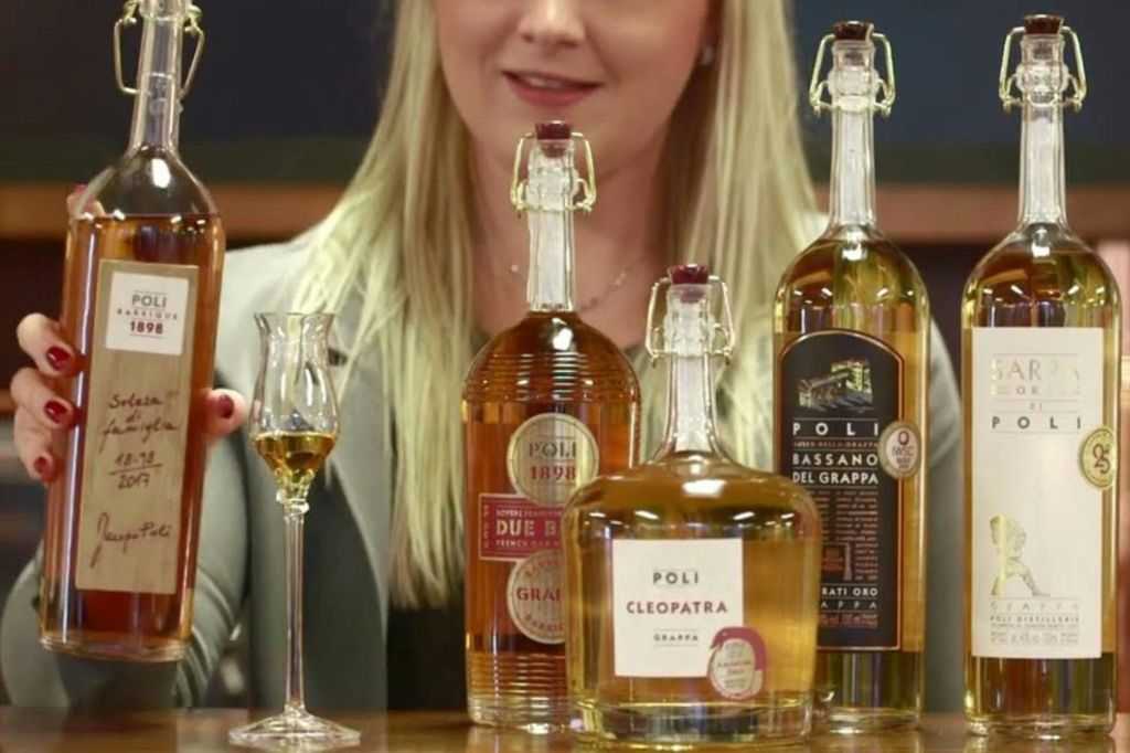 폴리 클레오파트라, 두에 바릴리, 바사노 델 그라파 등 폴리 그라파 3병 뒤에 한 여성이 그라파 한 잔을 들고 있습니다.