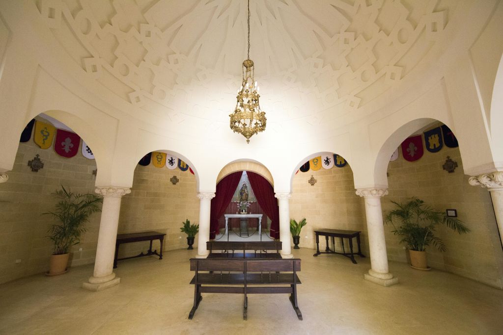 아치형 출입구, 샹들리에, 벤치, 붉은 커튼, 화분, 장식용 깃발이 놓인 제단이 있는 작은 예배당입니다.