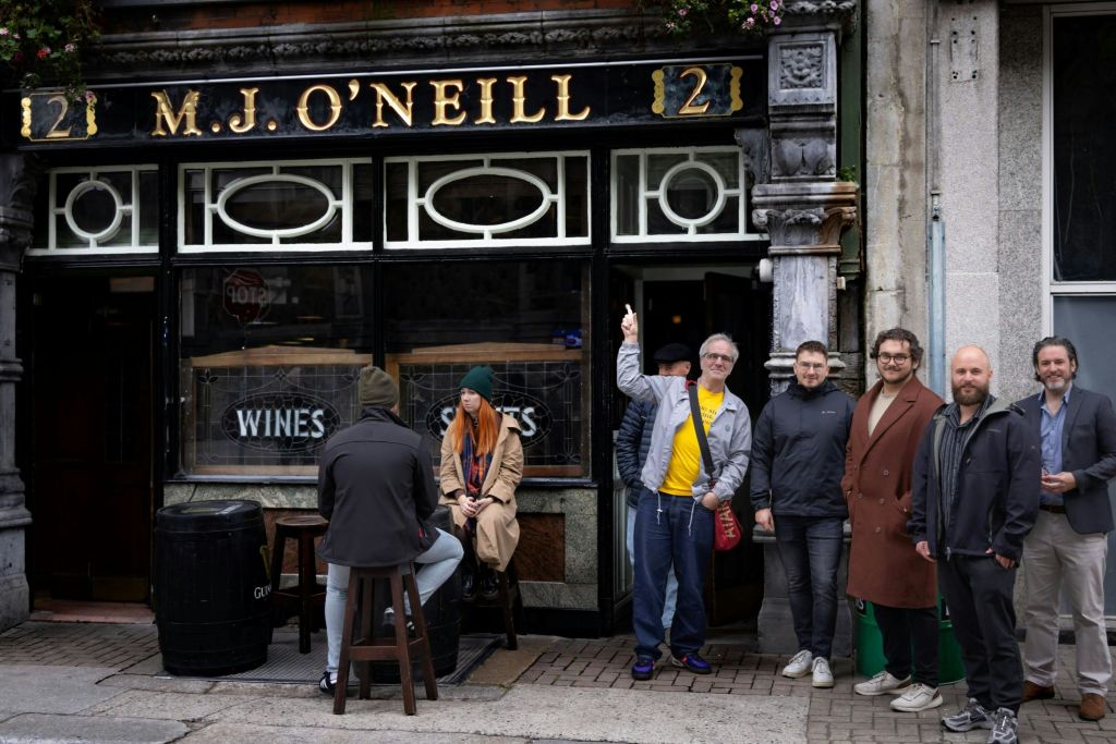 한 무리의 사람들이 "O 'Neill 21" 이라고 적힌 표지판이 있는 술집 밖에 서서 앉아 있습니다.