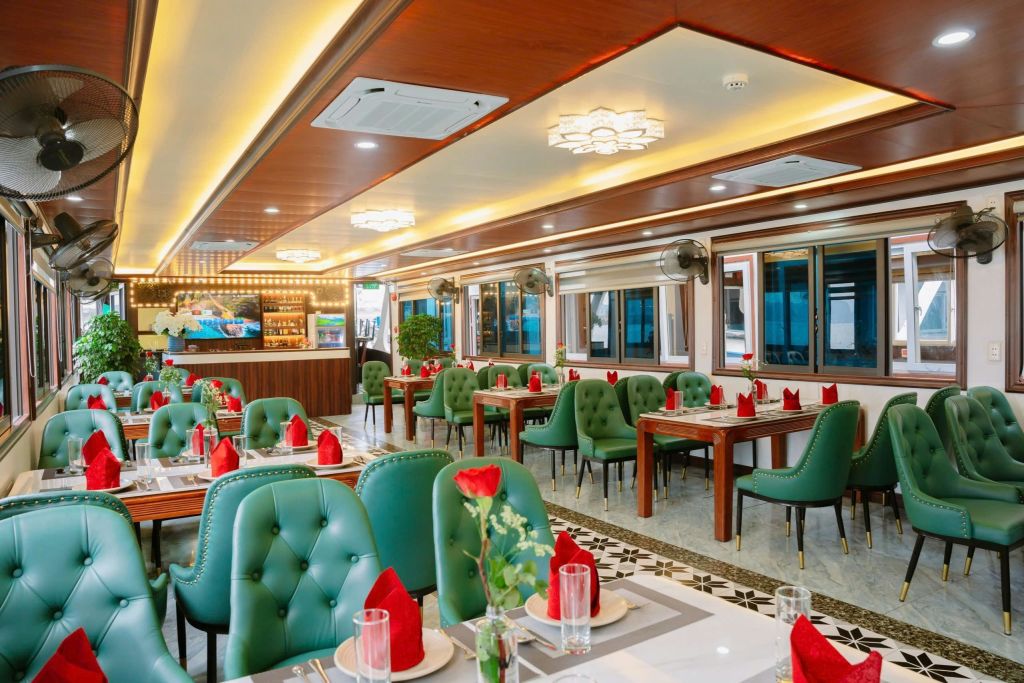 녹색 터프팅 의자, 빨간 냅킨과 유리 제품으로 세팅된 나무 테이블, 샹들리에의 따뜻한 조명이 있는 우아한 레스토랑 내부.