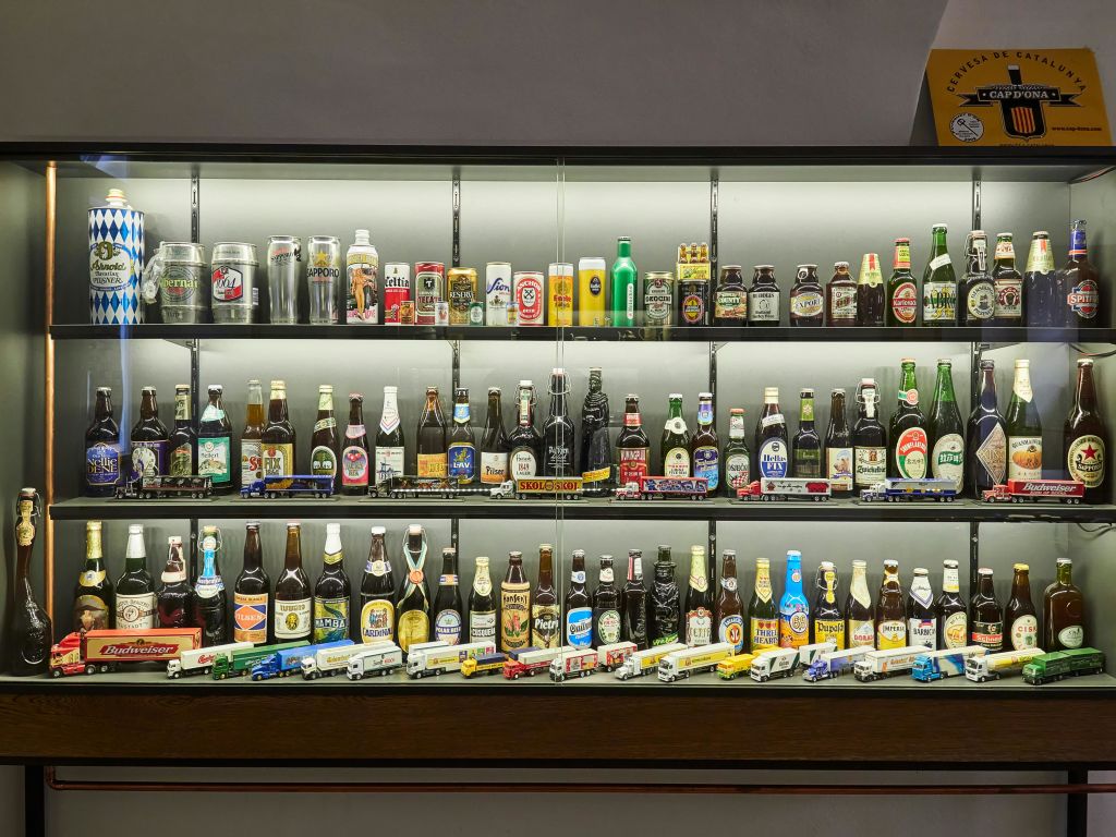 다양한 병과 맥주 캔이 담긴 3개의 선반이 있는 디스플레이 케이스, 하단의 미니어처 트럭.