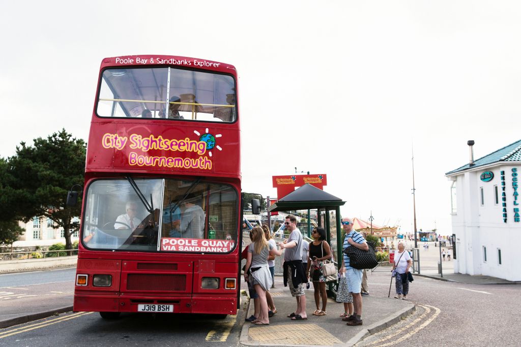 버스 정류장에서 '본머스 시내 관광' 이라고 적힌 빨간색 2층 관광 버스에 탑승하기 위해 사람들이 줄을 서서 기다립니다.