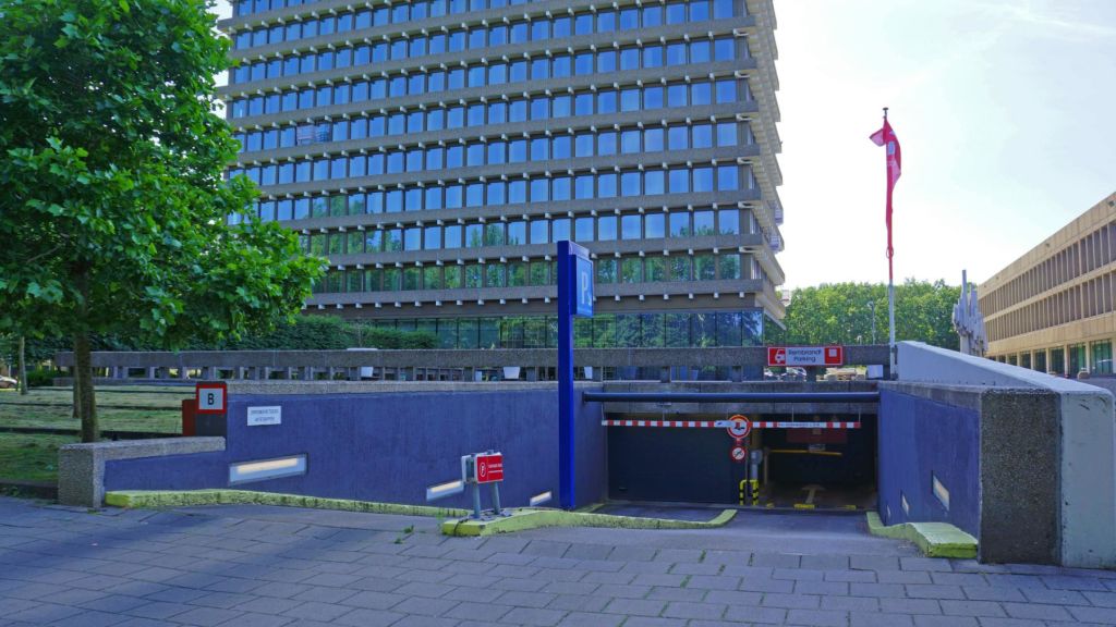 반사창문, 지하주차장 입구, 간판, 왼쪽에 나무 몇 그루가 있는 복층 건물입니다.