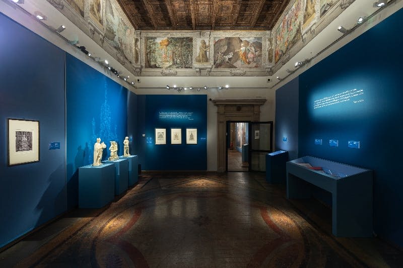 갤러리에는 나무 천장과 스포트라이트가 있는 밝은 색상의 벽에 세 개의 추상적이고 어두운 톤의 조각이 설치되어 있습니다.