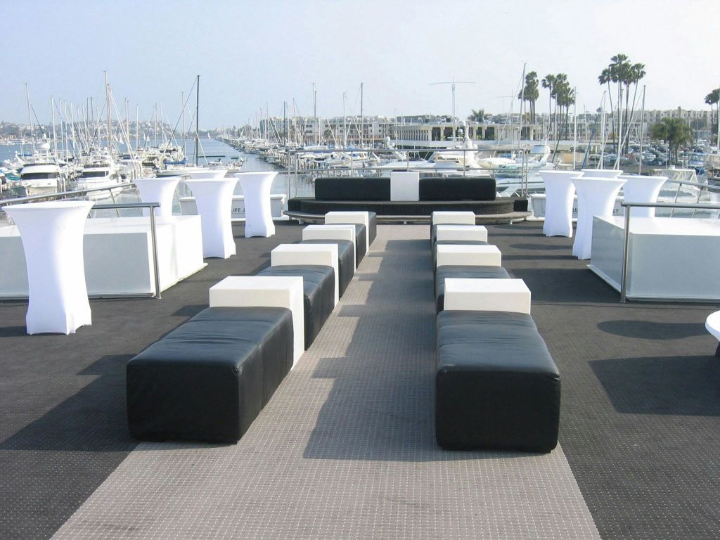 검은색과 흰색 오토만, 흰색 칵테일 테이블, 수많은 선착장이 있는 정박지 전망이 있는 야외 좌석 공간.