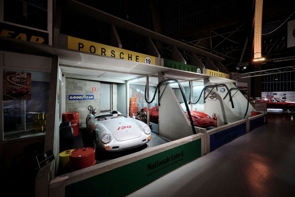 빈티지 포르쉐, 재규어, 페라리 경주용 자동차는 도구, 타이어, 스폰서 사인이 있는 복고풍 차고에 전시되어 있습니다.