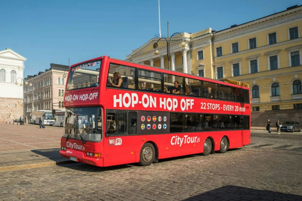 유서 깊은 건물을 배경으로 자갈길에 '홉온 홉오프 (Hop-On Hop-Off)' 라는 이름의 빨간색 2층 버스가 주차되어 있습니다.