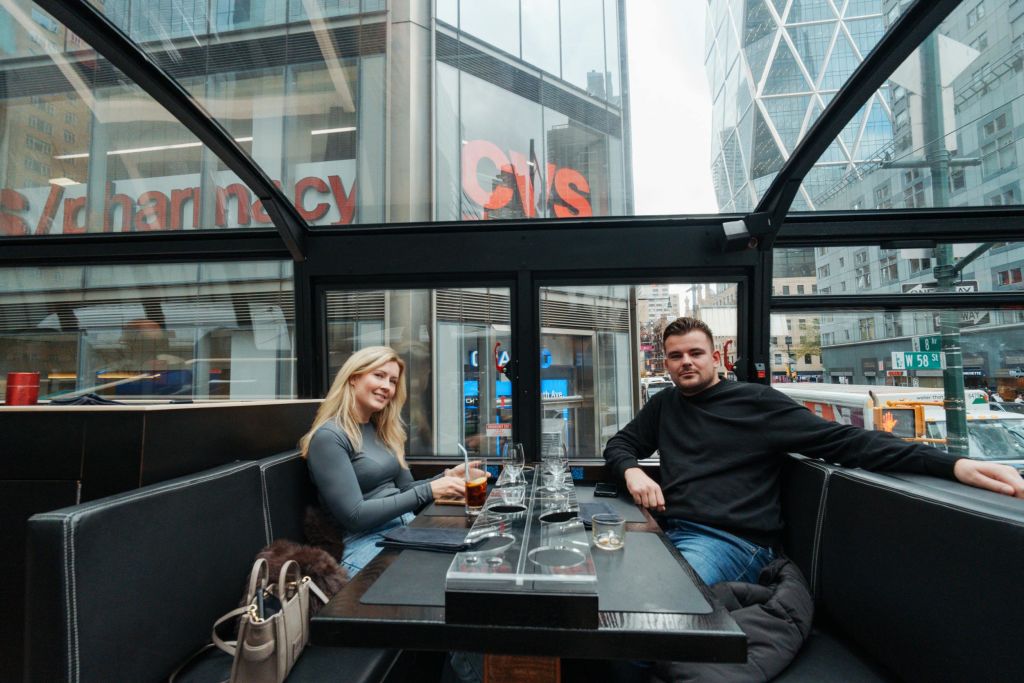 CVS 매장을 비롯하여 도시 건물을 배경으로 유리로 둘러싸인 레스토랑에 앉아 있는 두 사람.