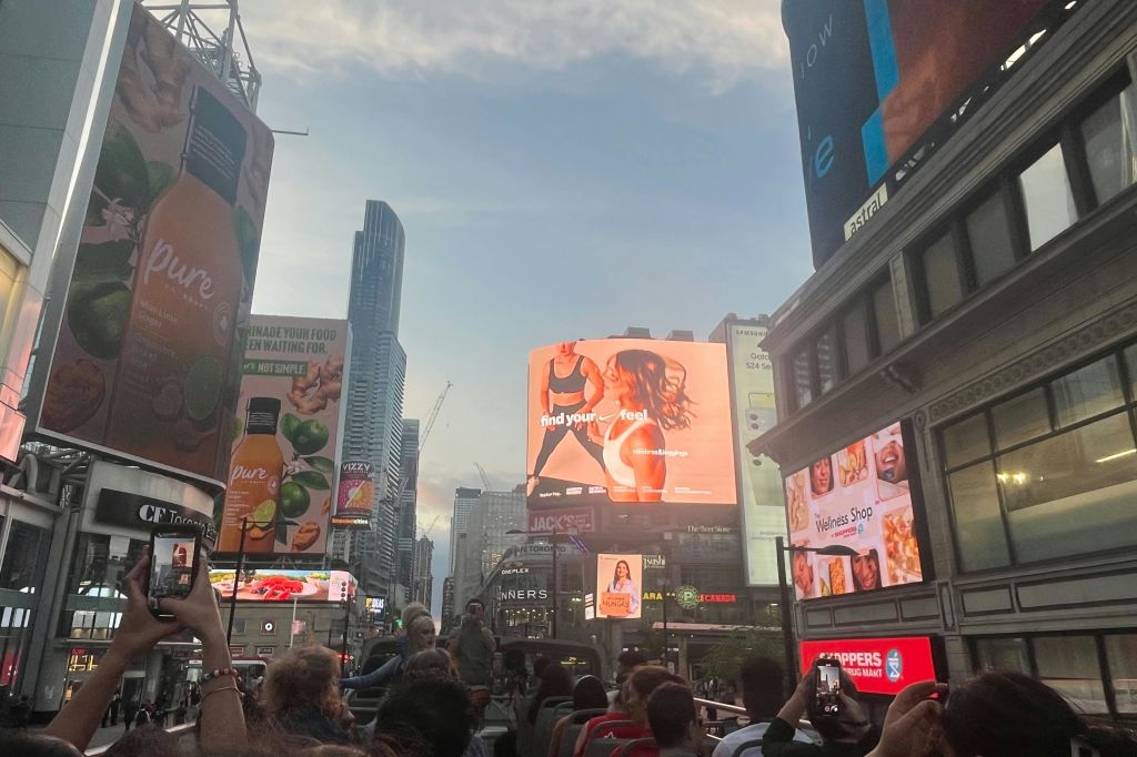 영-던다스 스퀘어에 접근하는 탑 더블 데커 투어 버스를 엽니다. 광고를 보여주는 여러 광고판 및 TV 화면.