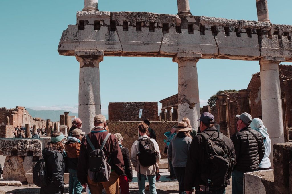 배낭과 모자를 쓴 관광객들이 맑고 푸른 하늘 아래 고대 석조 유적을 관찰합니다.