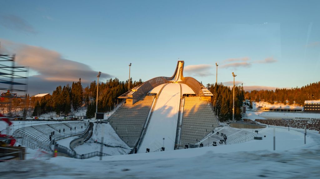 해질 무렵 눈 덮인 경사로와 나무로 둘러싸인 투광 조명으로 조명이 켜진 스키 점프.