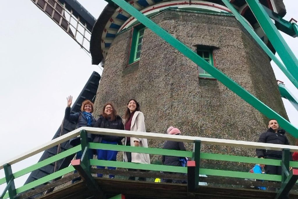 세 사람이 풍차 발코니에 서서 카메라를 보며 미소를 짓고 있습니다. 하늘이 흐리다.